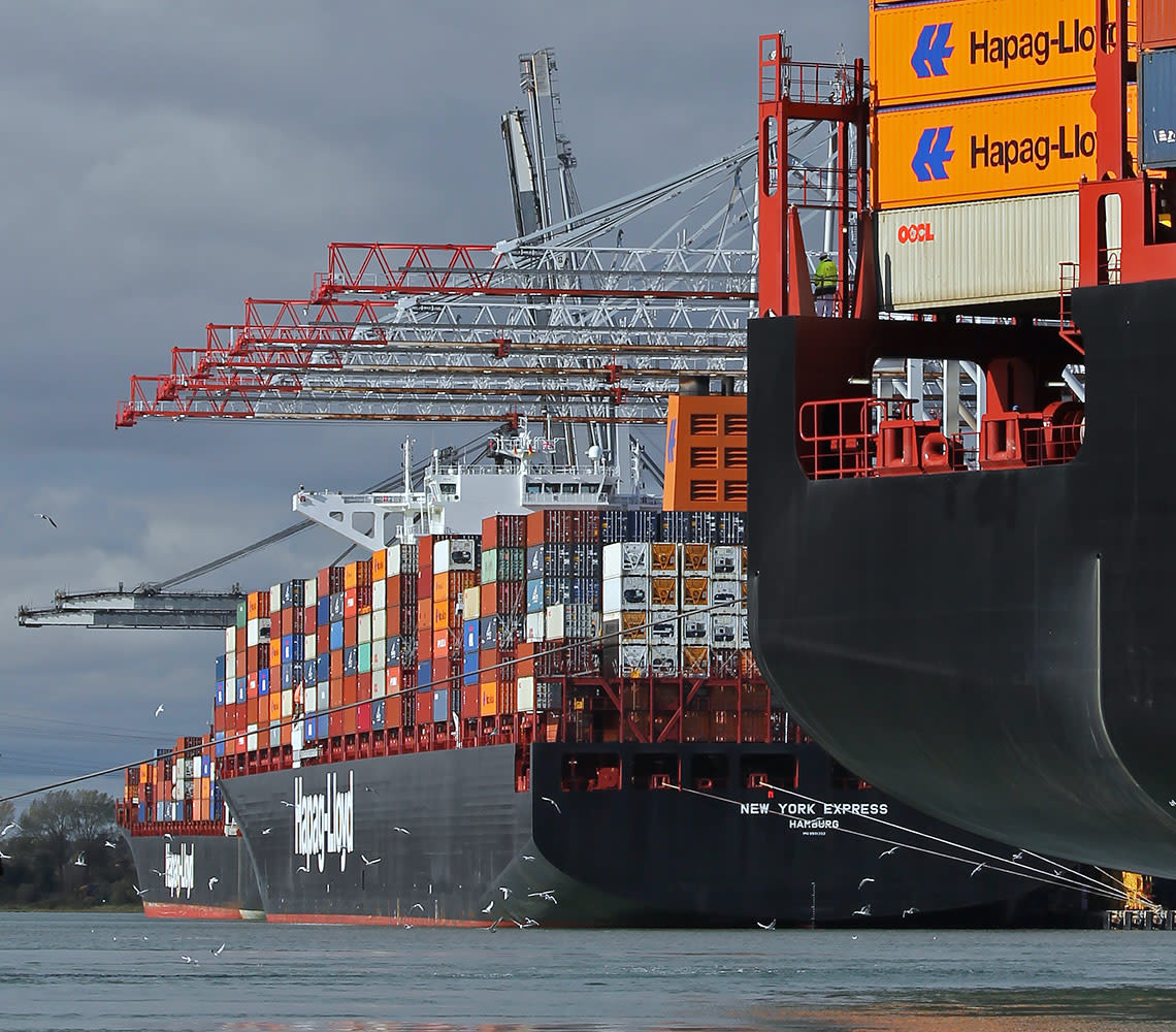 A large Hapag-Lloyd cargo ship equipped with a crane, docked and ready for loading and unloading operations.